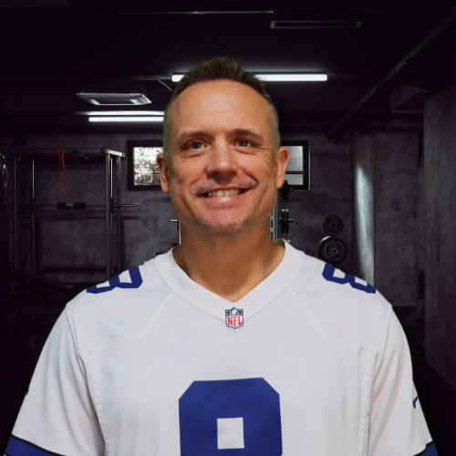 Man in a Dallas Cowboys jersey smiles in a basement gym with weights.