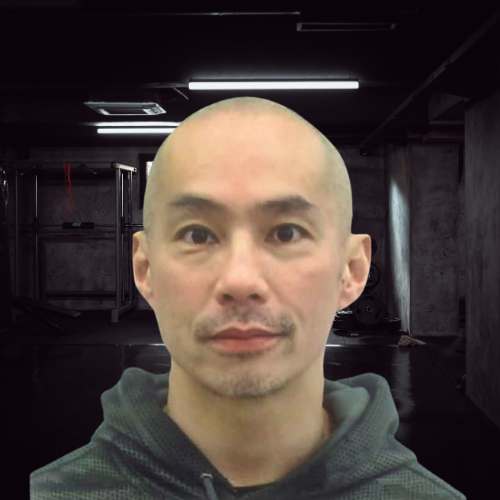 Man with shaved head and mustache in front of a dark, industrial-looking backdrop.