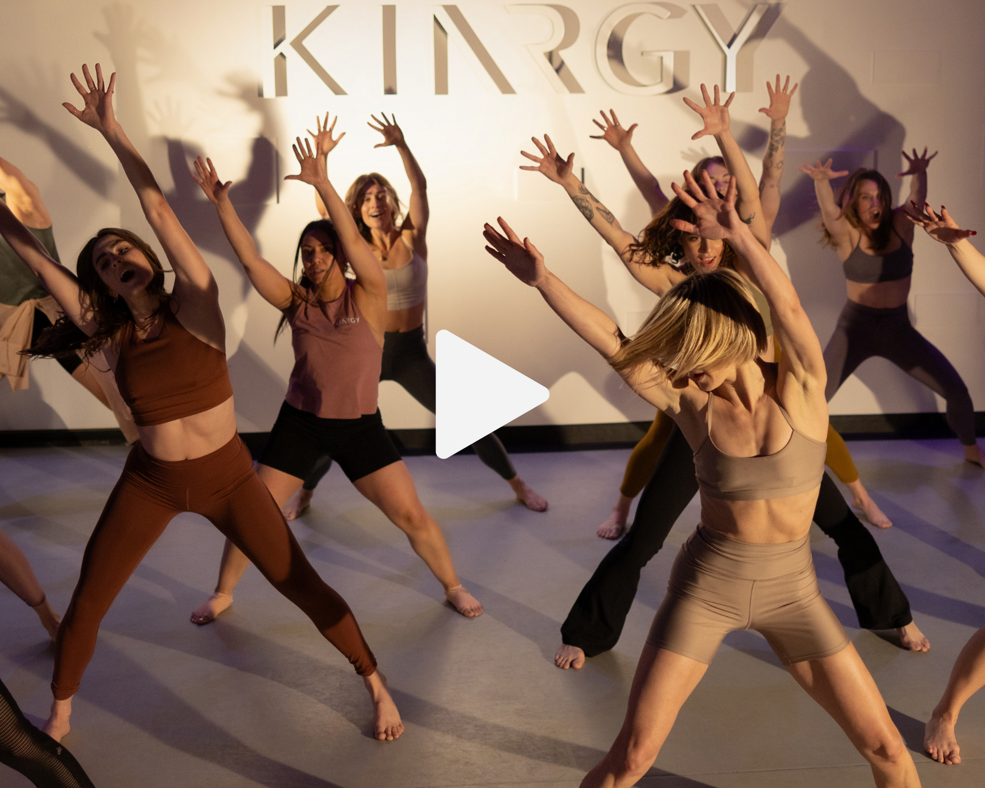 A group of women are dancing in front of a sign that says KINRGY.