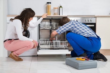 Woman watches as a repairman works on a dishwasher in a kitchen.