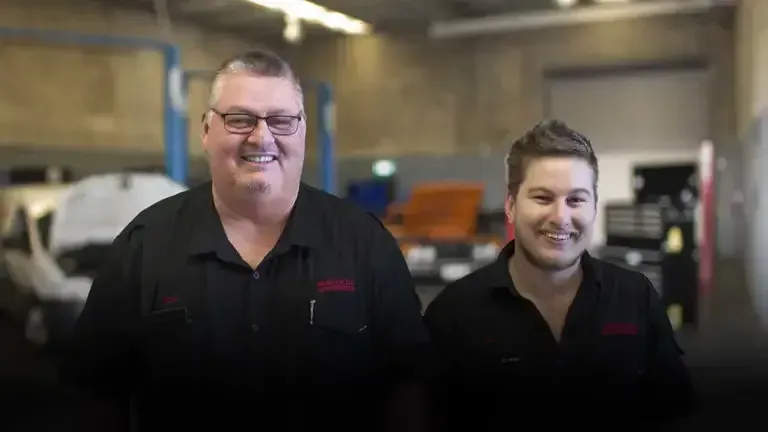 Two men are standing next to each other in a garage and smiling. — Maroochy Automotive in Kunda Park, QLD