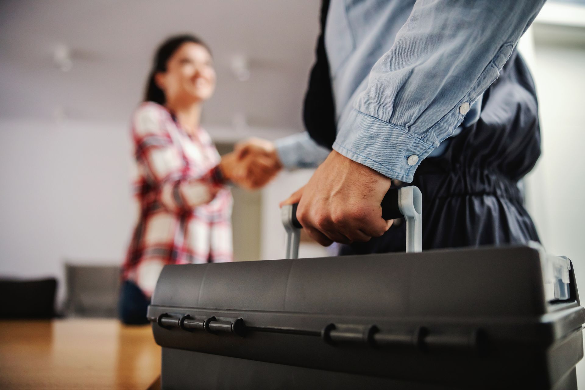 Close-up of a home plumbing contractor holding his toolbox while shaking hands with a woman.