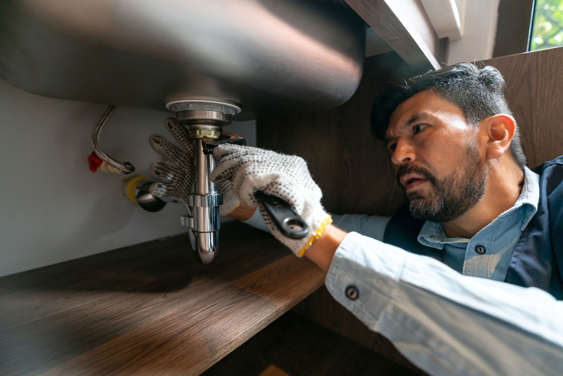 Plumber fixing a leak in the kitchen sink of a house.