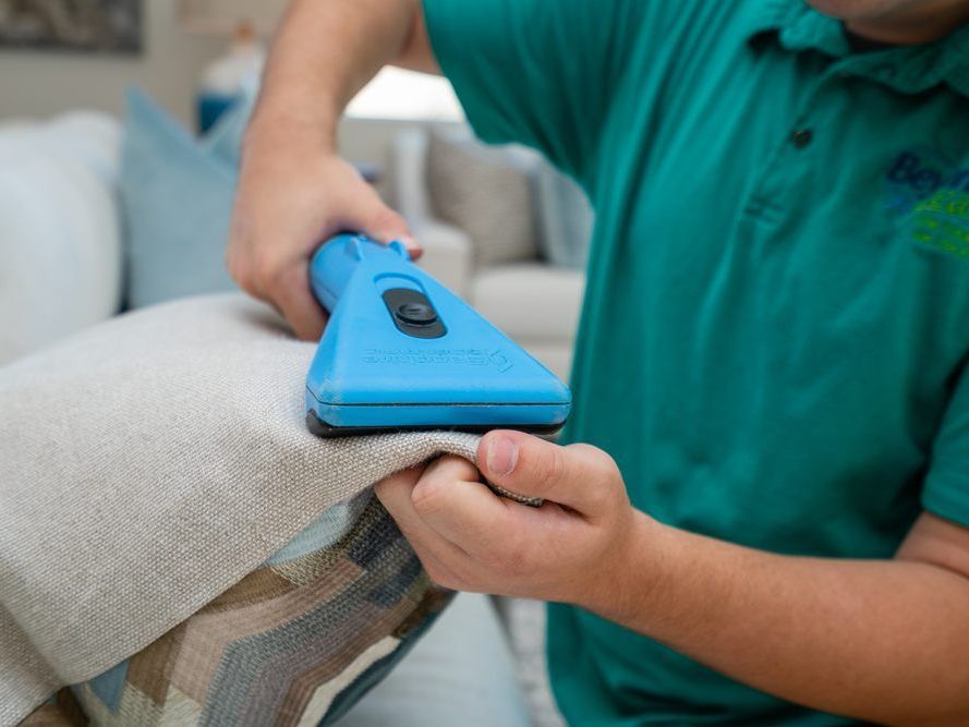 a man in a green shirt is using a blue vacuum cleaner on a couch