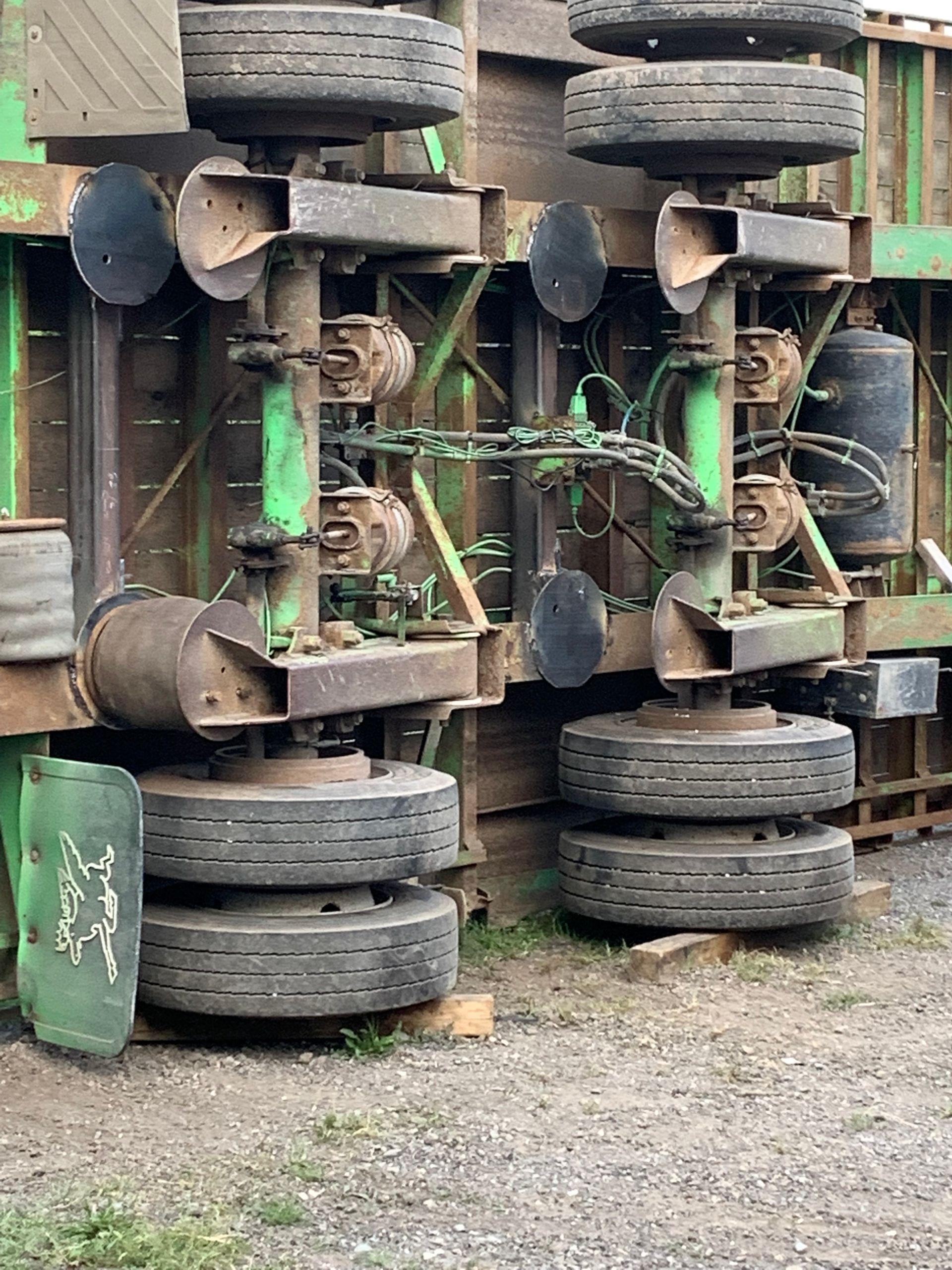 Deux essieux de semi-remorque verts renversés, les pneus reposant au sol, probablement suite à un accident.