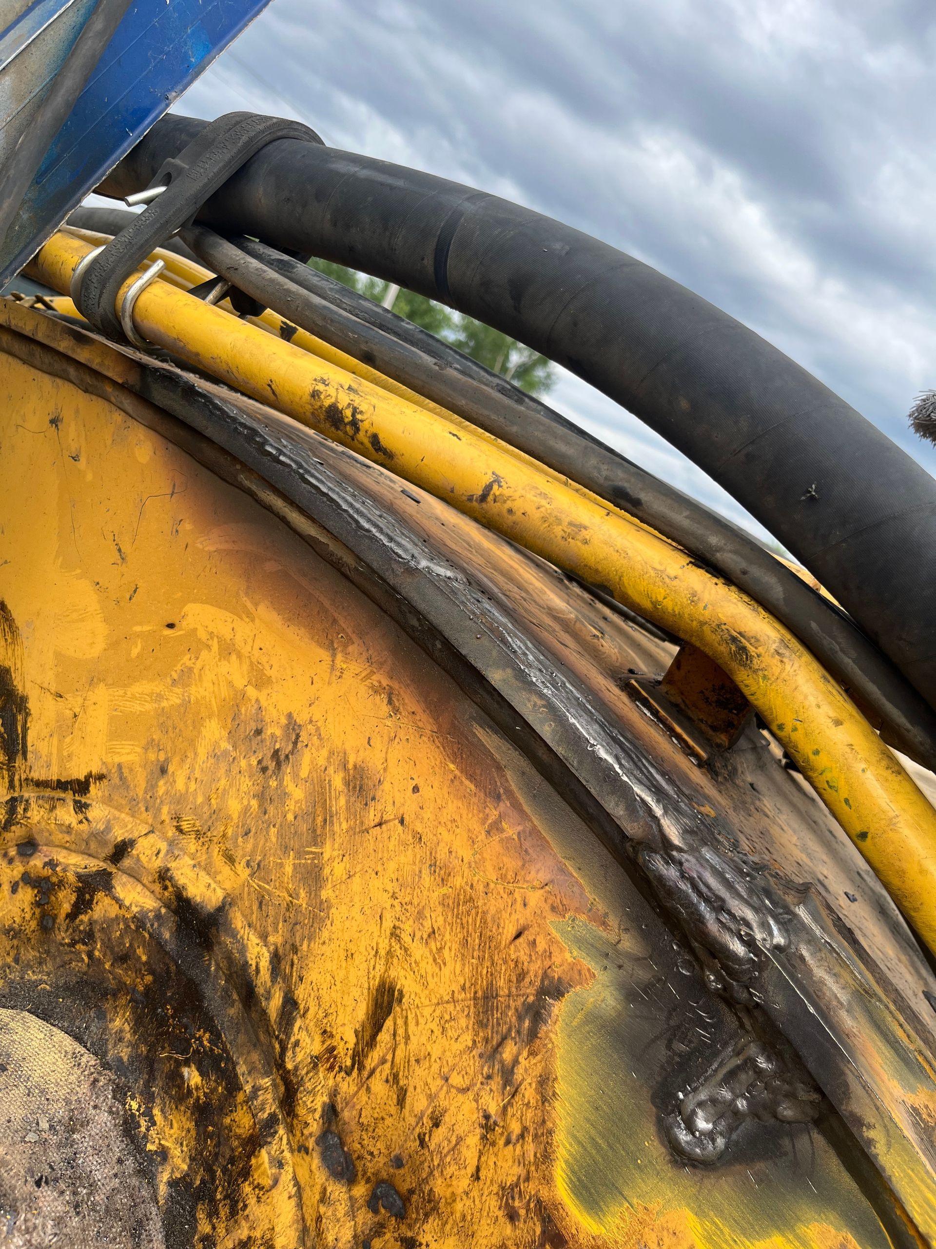 Gros plan sur une pièce de machine jaune et endommagée, laissant apparaître les soudures, les tuyaux et le câblage.