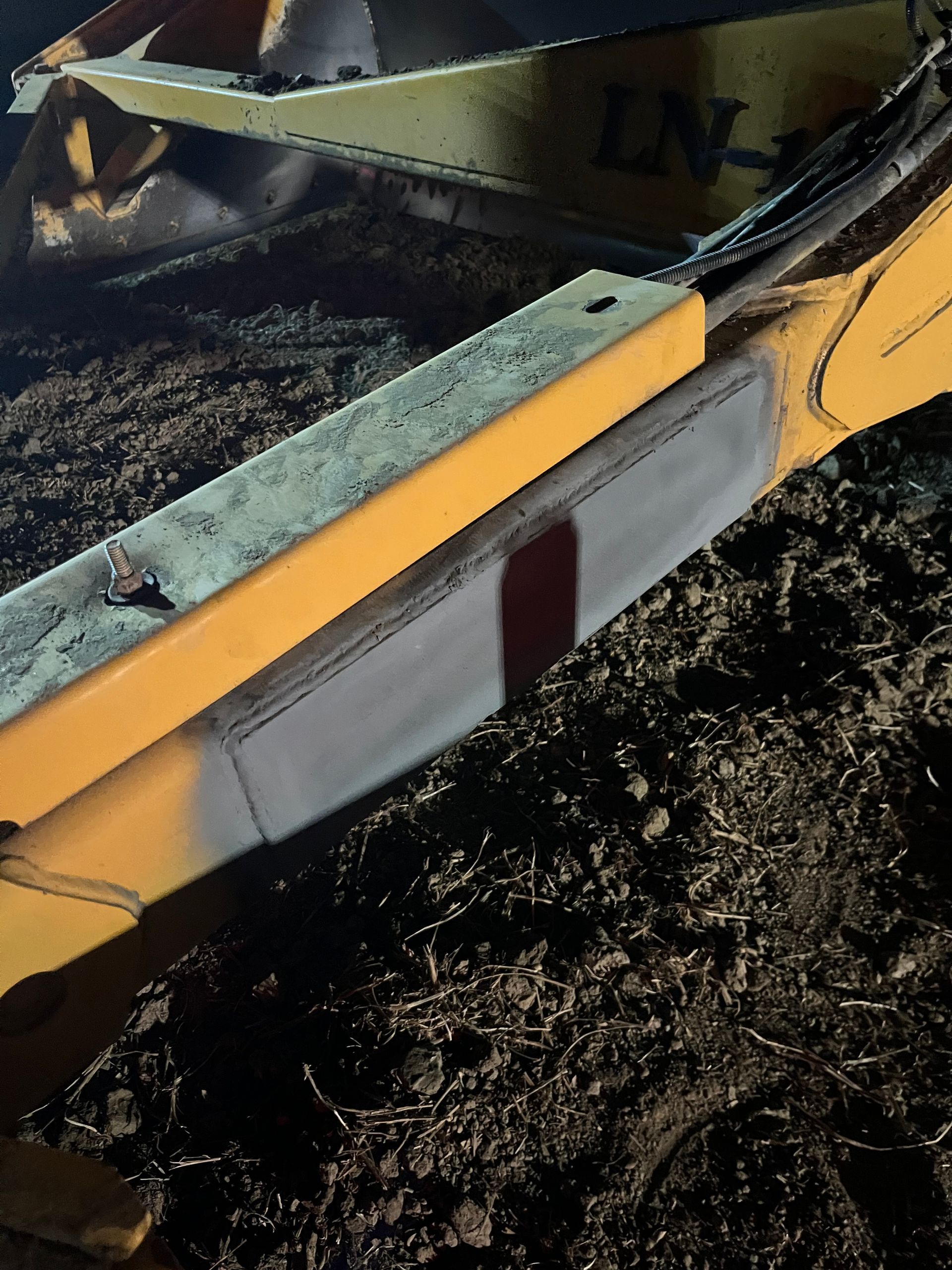 Bras d'excavatrice jaune et gris dans un décor sombre et poussiéreux, avec une bande rouge.