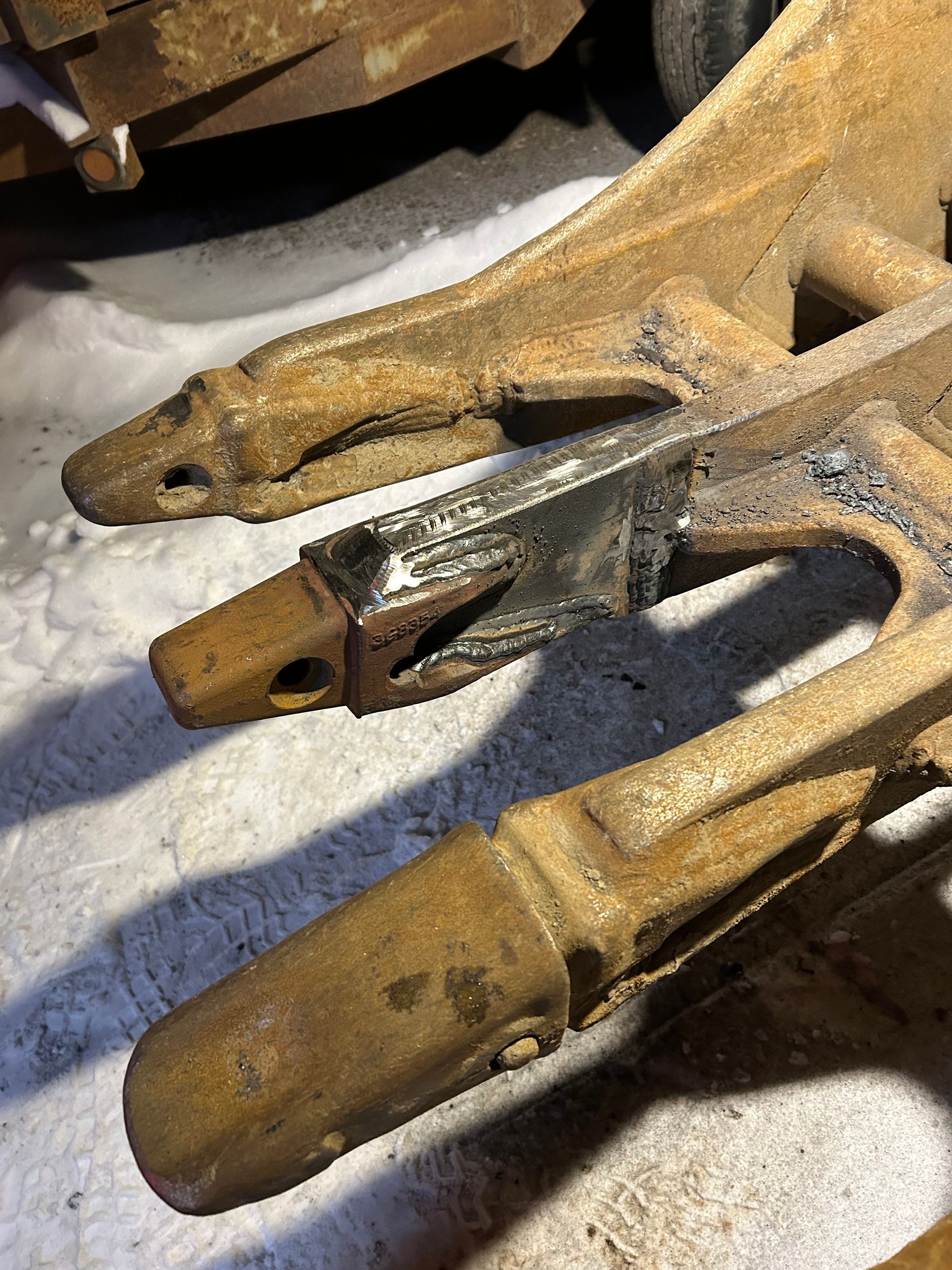 Trois dents en métal rouillé, dont une récemment soudée, gisent sur un sol enneigé.