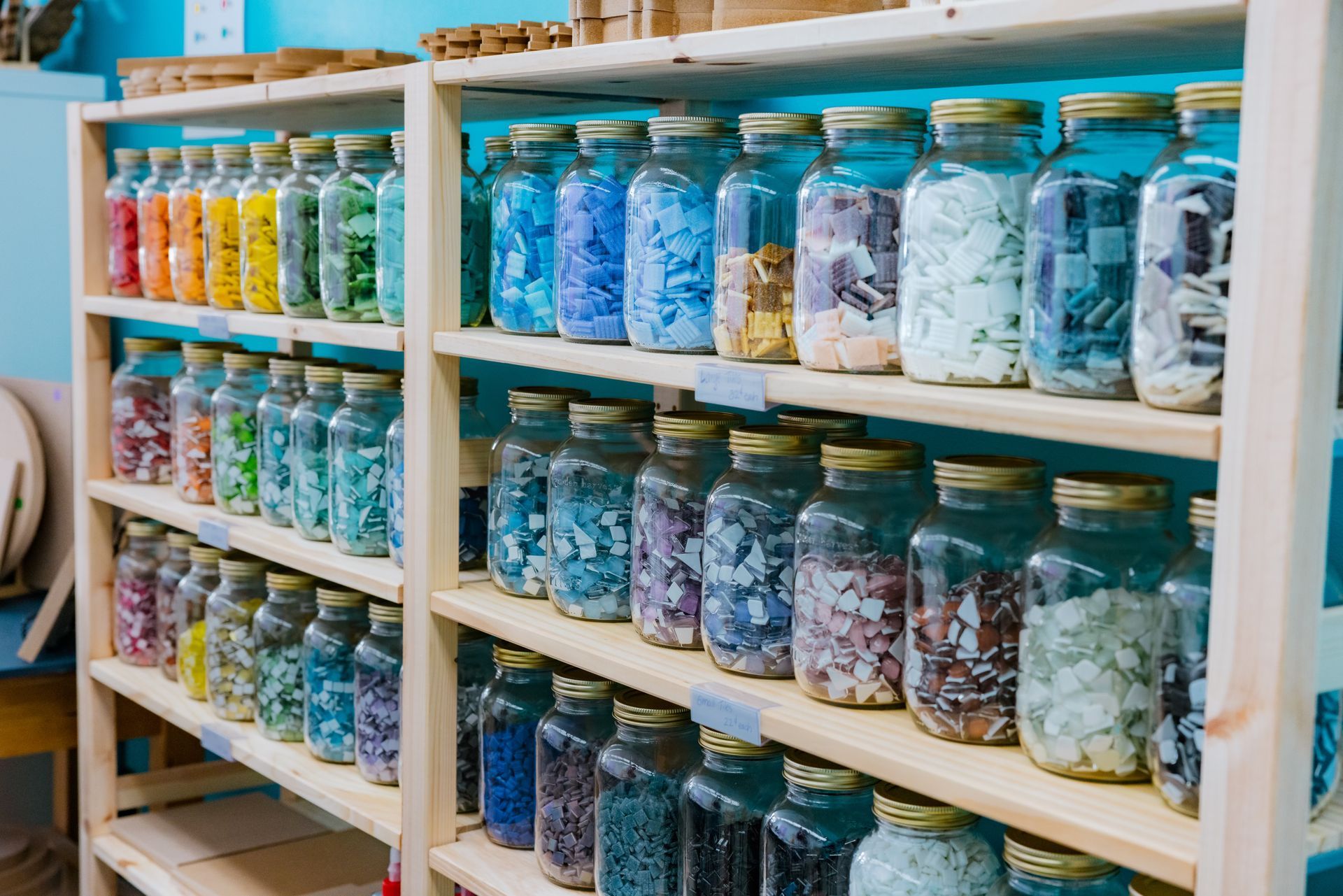 A shelf filled with jars filled with different colored mosaic tiles.