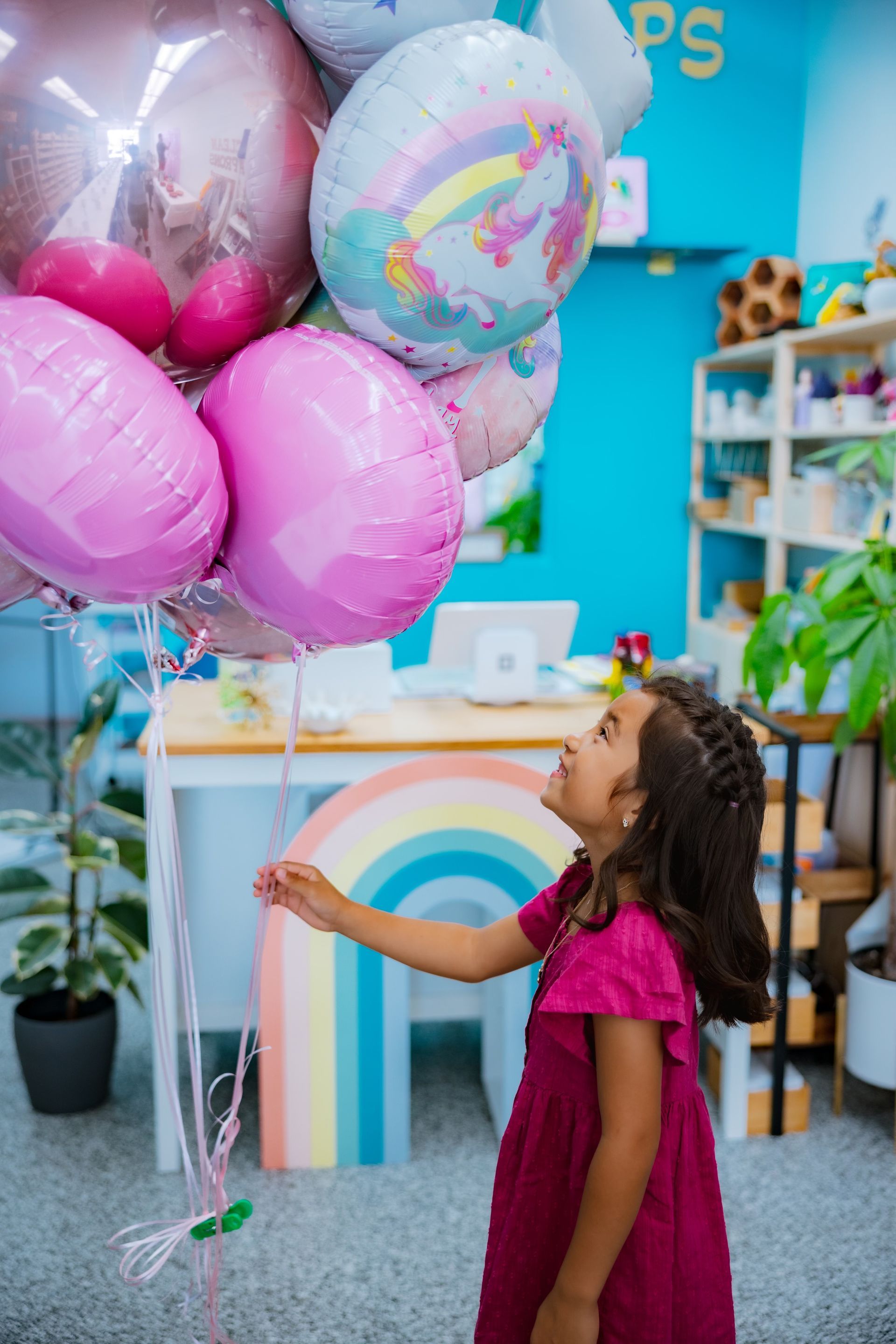 A little girl is holding a bunch of pink balloons in a room.