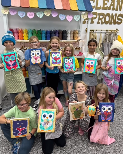 A group of children are posing for a picture while holding owl paintings. Each painting is a unique take on the same owl.