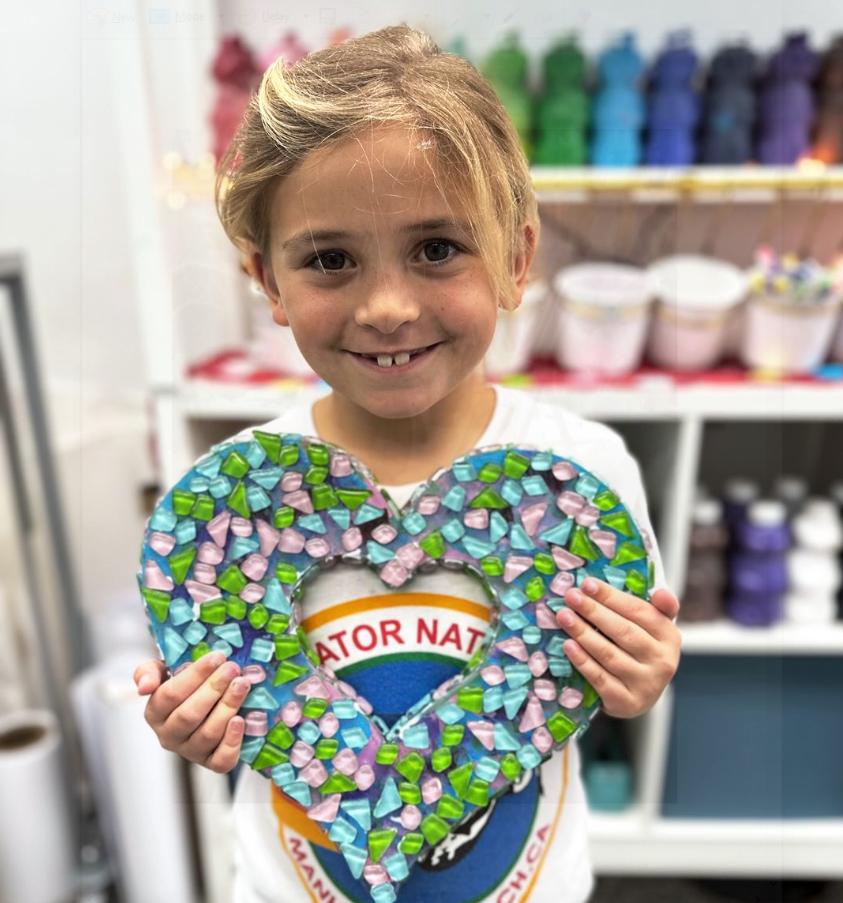 A young girl is posing for a picture. She is holding a mosaic heart.