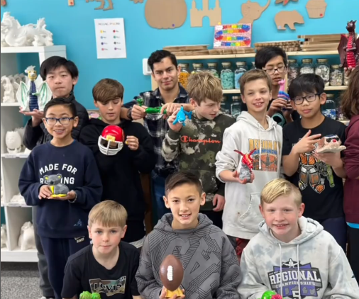 A group of young boys are posing for a picture in a room. Each boy is holding up a painted ceramic creation. These ceramics range from a football helmet, a koala, a dragon to an airplane.