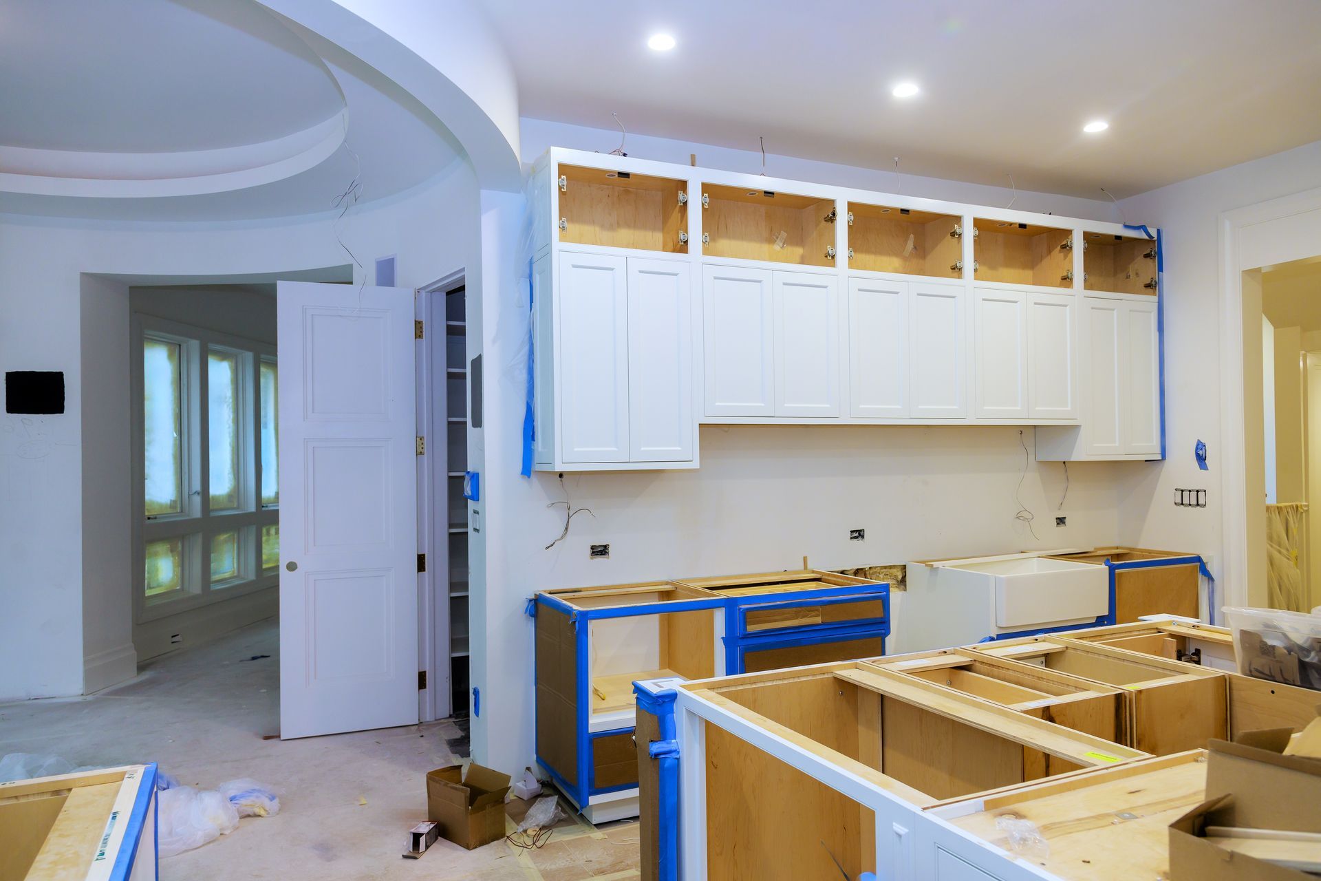 Kitchen under renovation with white cabinets, exposed wood framing, and construction materials on the floor