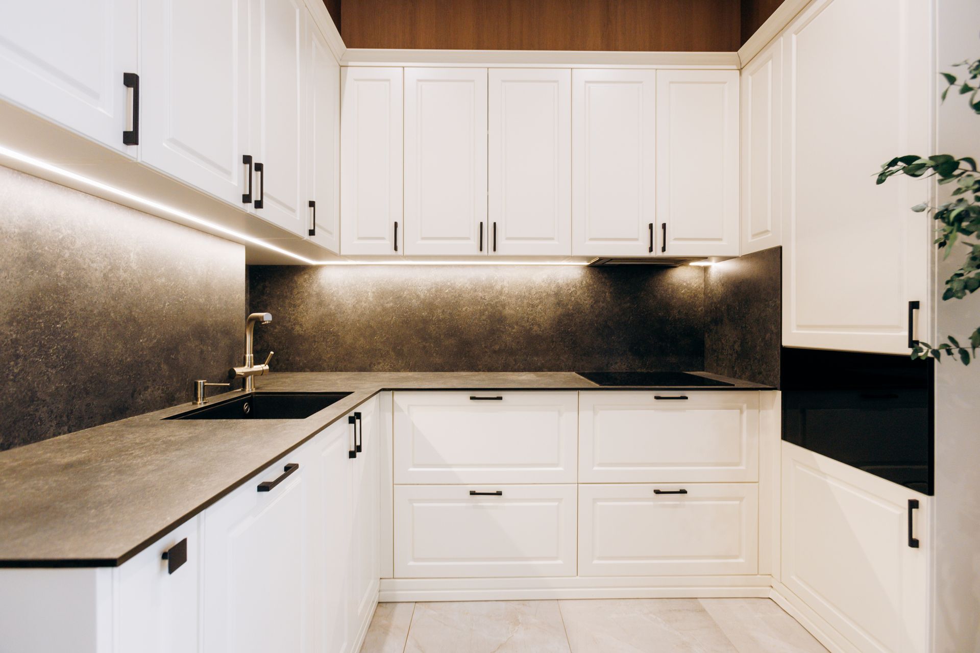 Modern white kitchen with black countertops, under-cabinet lighting, and dark backsplash Modern white kitchen with black countertops, under-cabinet lighting, and dark backsplash