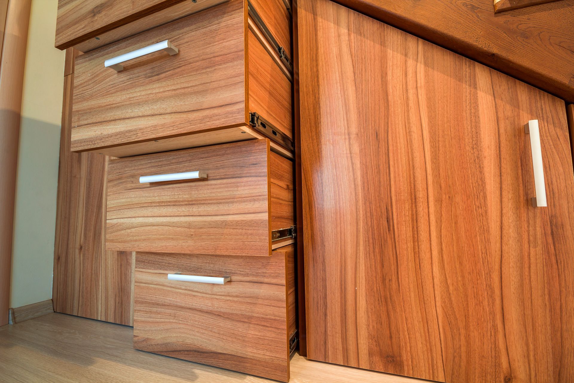Wooden kitchen cabinets with three drawers and a cabinet door, viewed close-up from floor level.