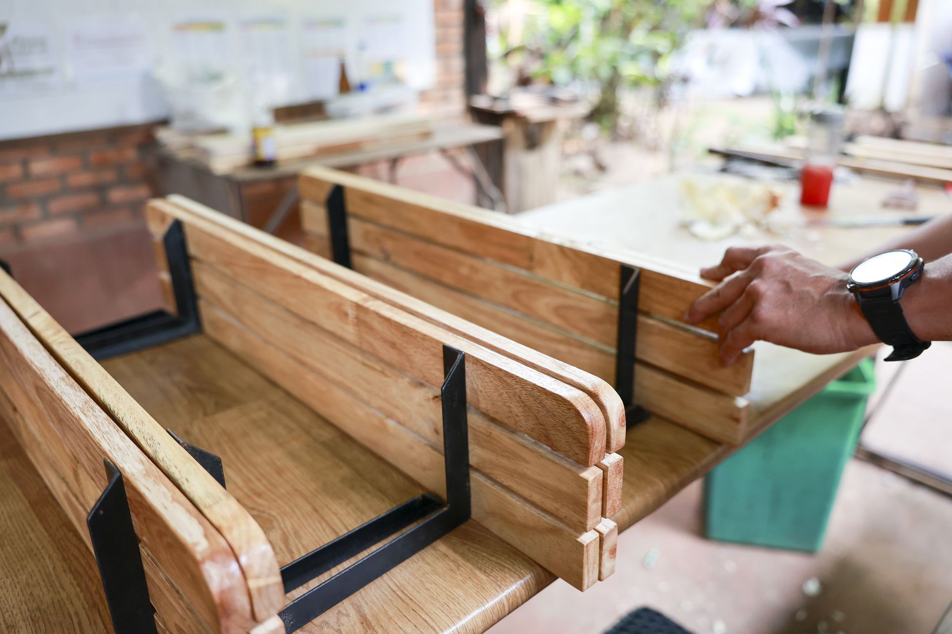 Wooden benches under construction in a workshop, with a hand adjusting one piece