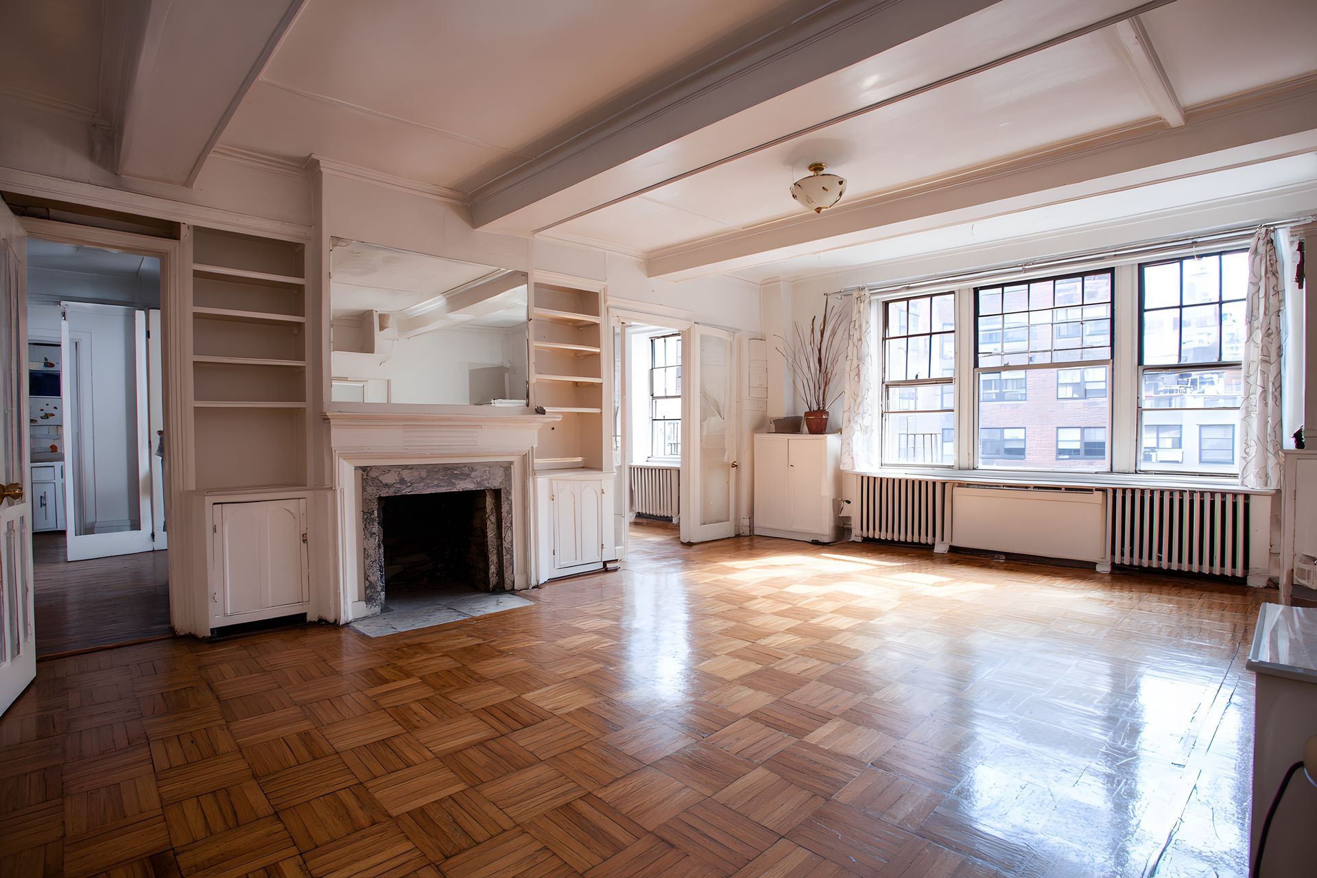 Empty sunlit living room with hardwood floors, fireplace, large windows, and white walls Empty sunlit living room with hardwood floors, fireplace, large windows, and white walls