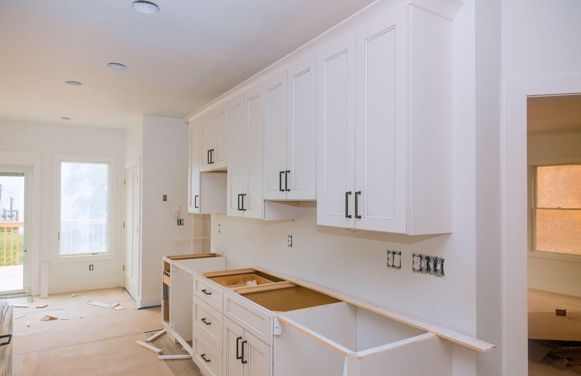 Bright white kitchen under renovation with unfinished cabinets, countertops, and flooring.