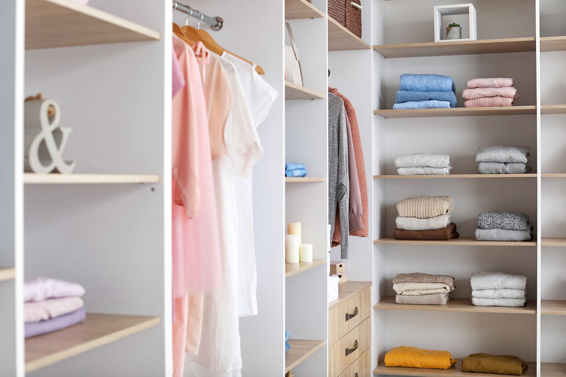 Open closet with hanging pastel clothes and neatly folded towels on shelves