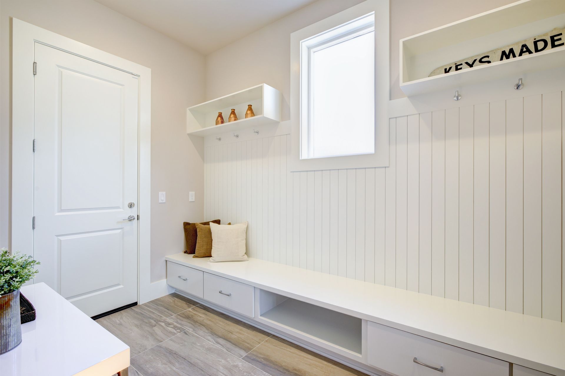 Bright mudroom with white bench, hooks, small window, and light wood floor