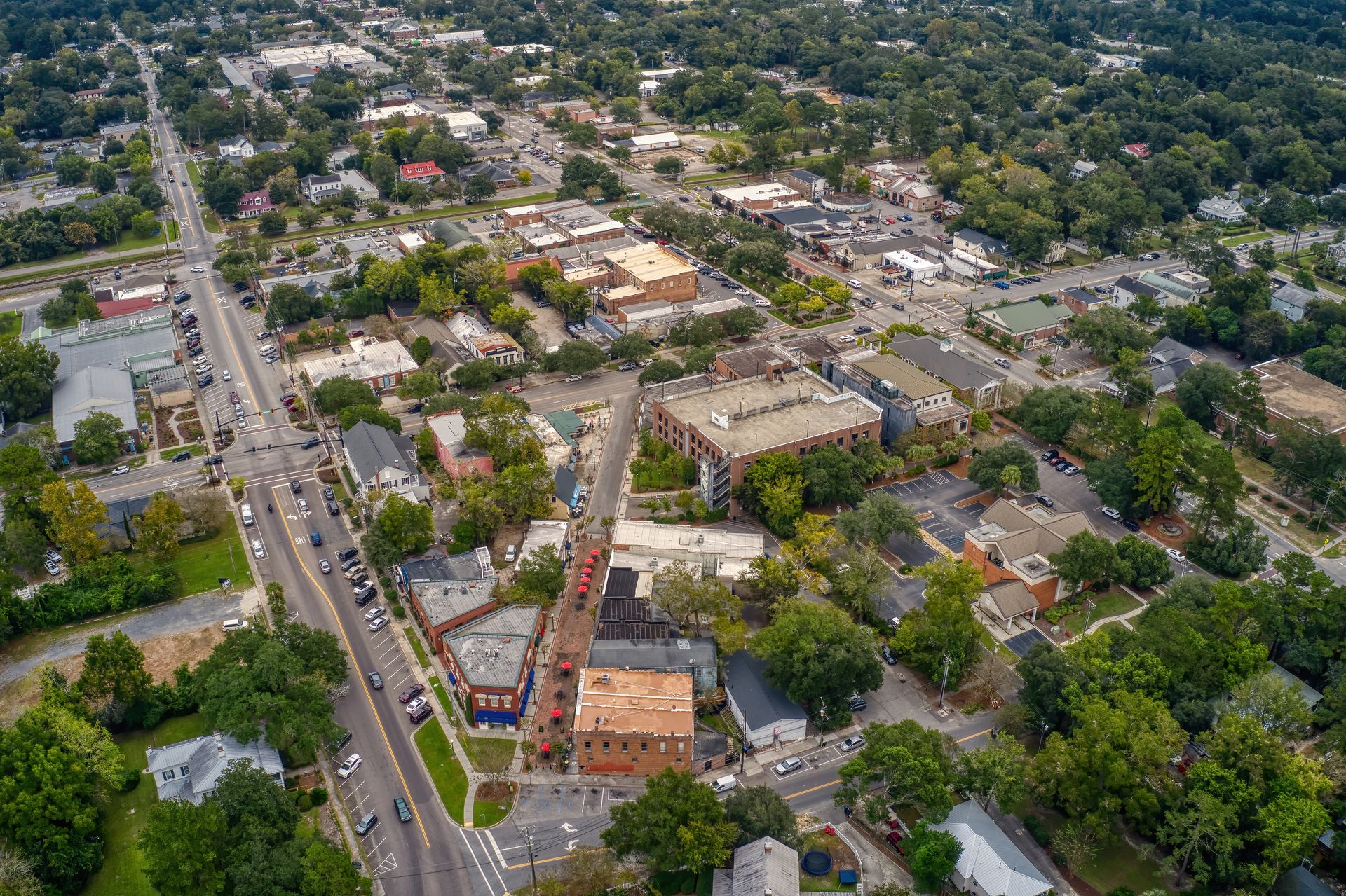 Aerial view of a suburban neighborhood with tree-lined streets, houses, and a busy road.