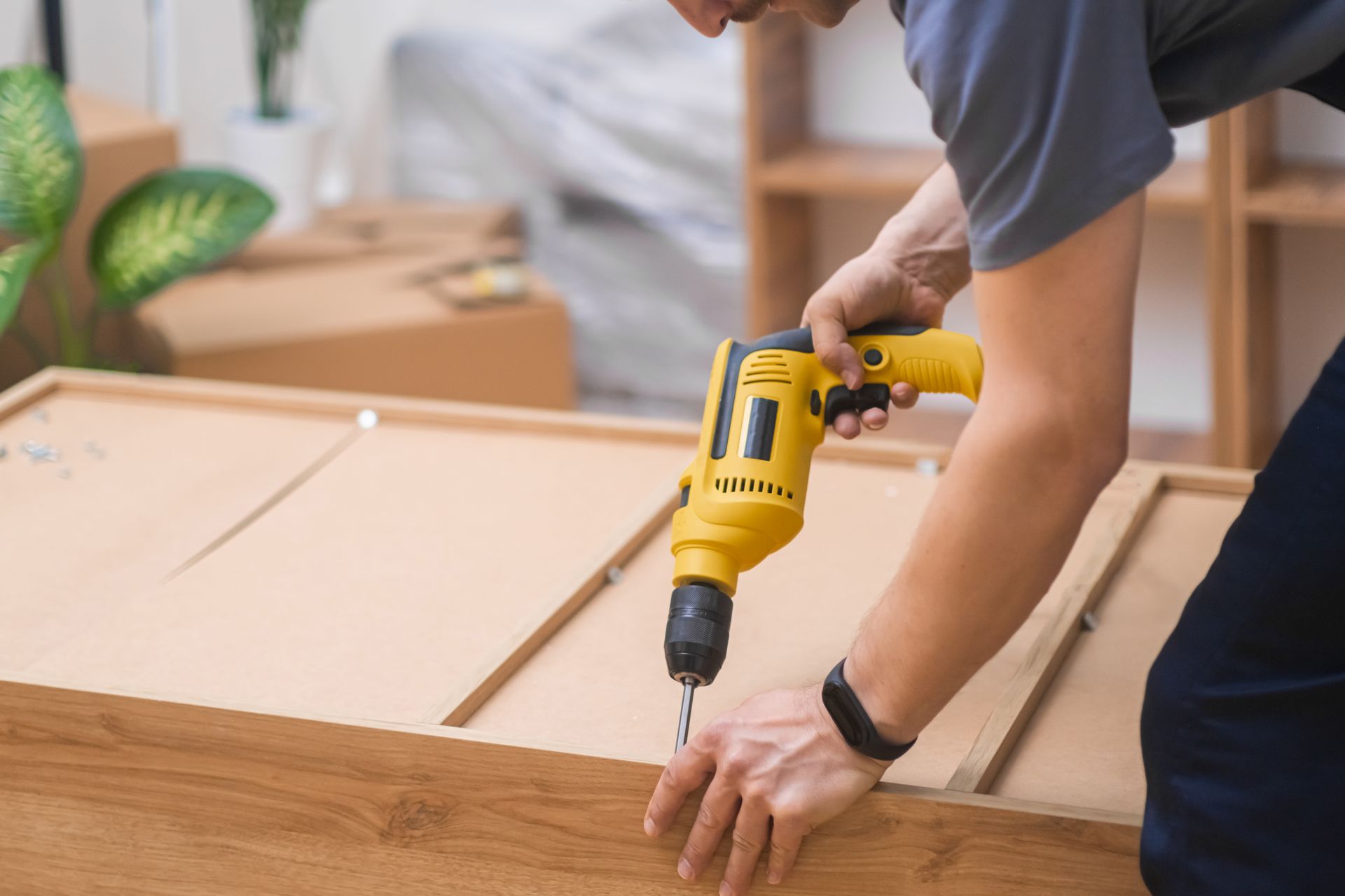 Person using a yellow power drill to assemble a wooden cabinet indoors