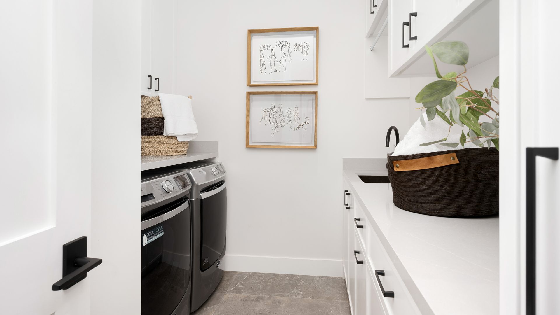 Narrow laundry room with a washer, dryer, white cabinets, and wall art.