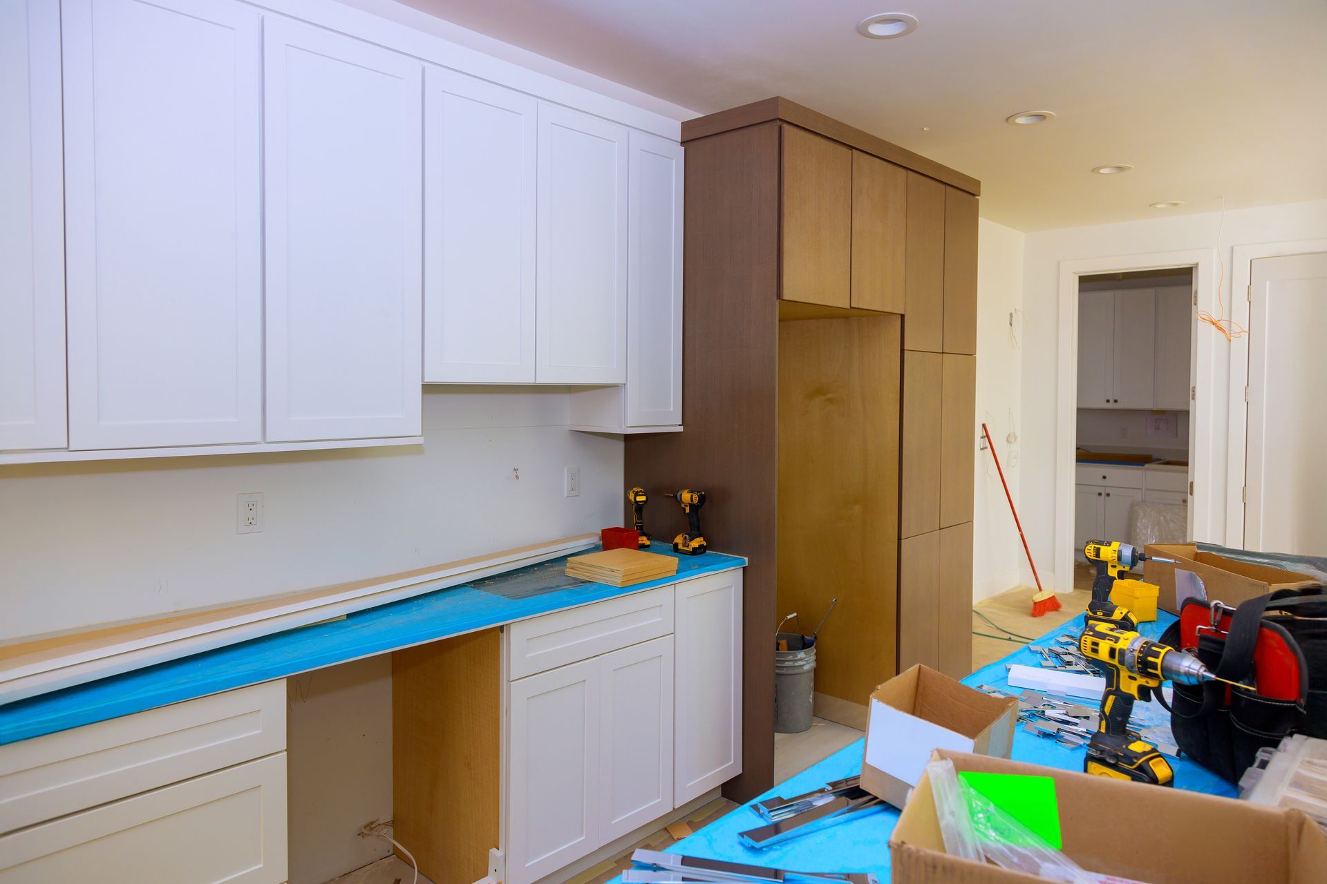 Partially renovated kitchen with white cabinets, wood pantry, tools, and materials scattered on counters and floor