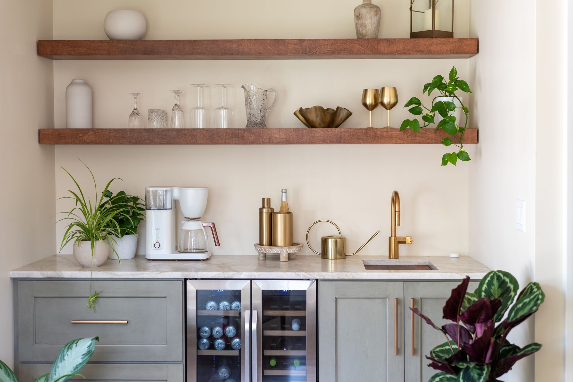 Modern kitchen coffee bar with wood shelves, espresso machine, gold accents, plants, and a wine fridge