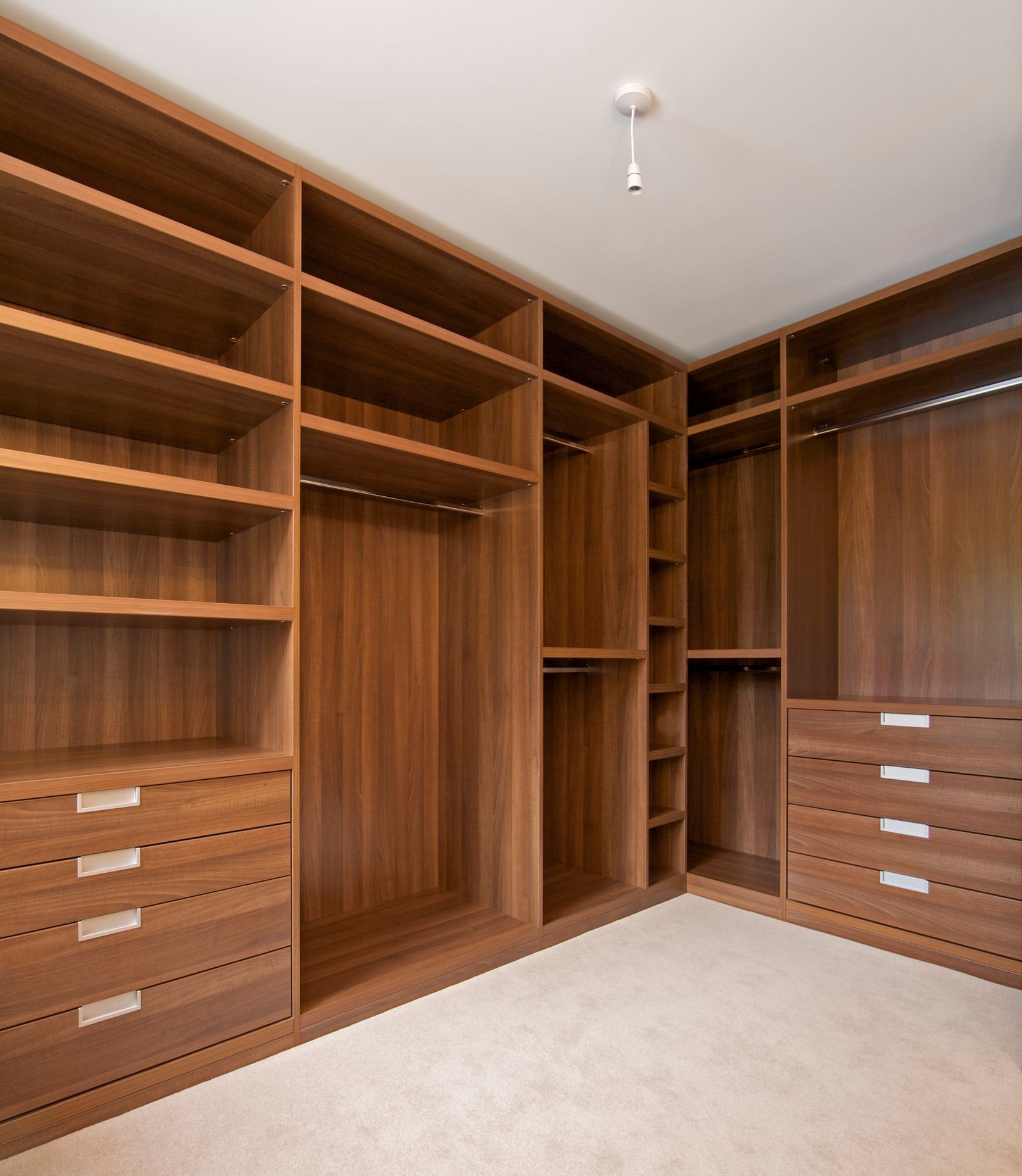 Empty walk-in closet with wooden shelves, hanging space, and drawers on beige carpet.