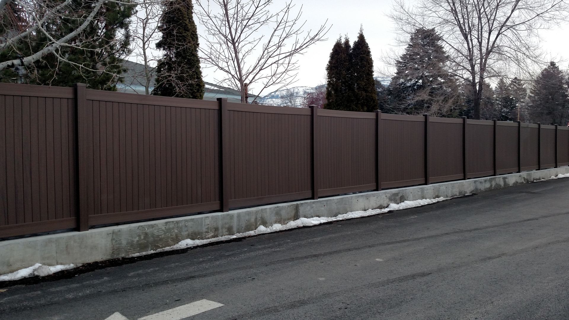 Long brown wooden fence along a roadside with bare trees in winter.