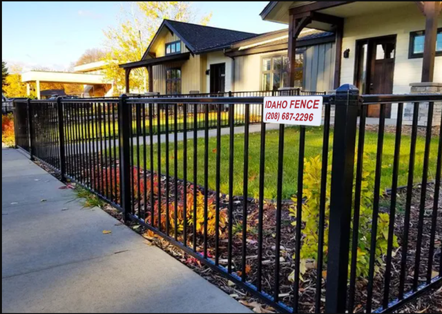 A black fence with a sign on it is in front of a house.