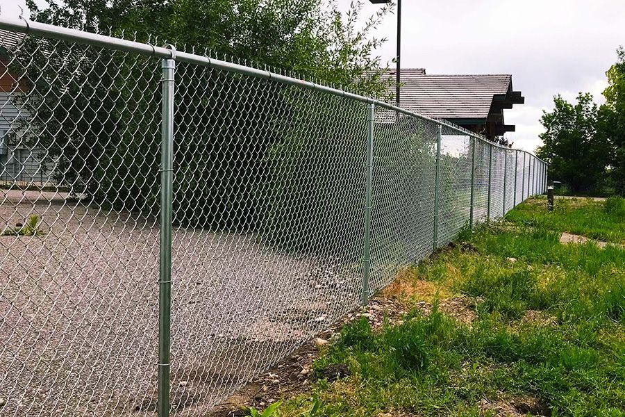 A chain link fence is surrounded by grass and gravel in front of a house.