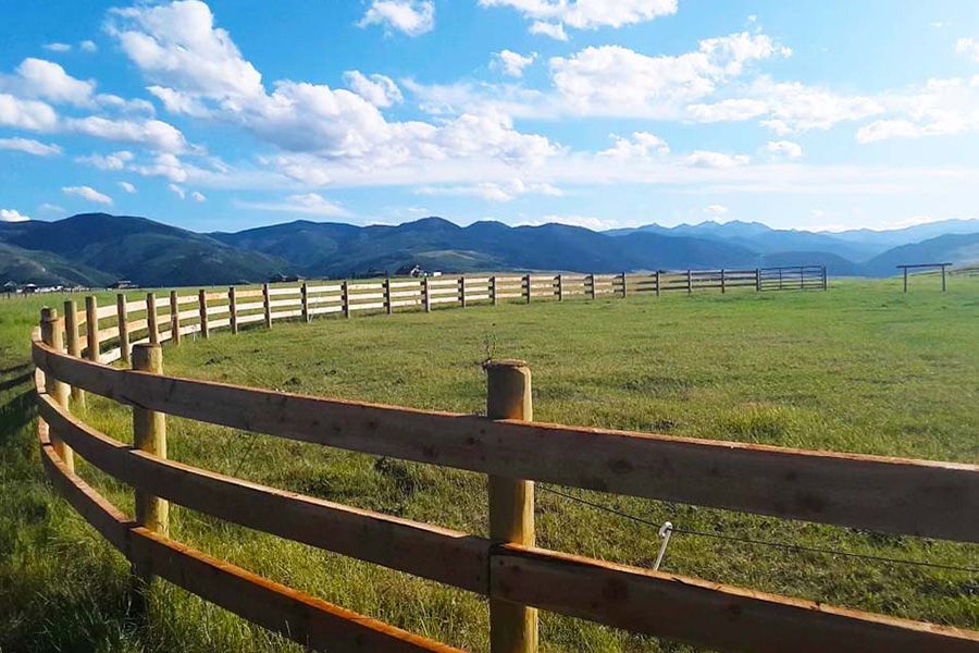 A wooden fence surrounds a grassy field with mountains in the background
