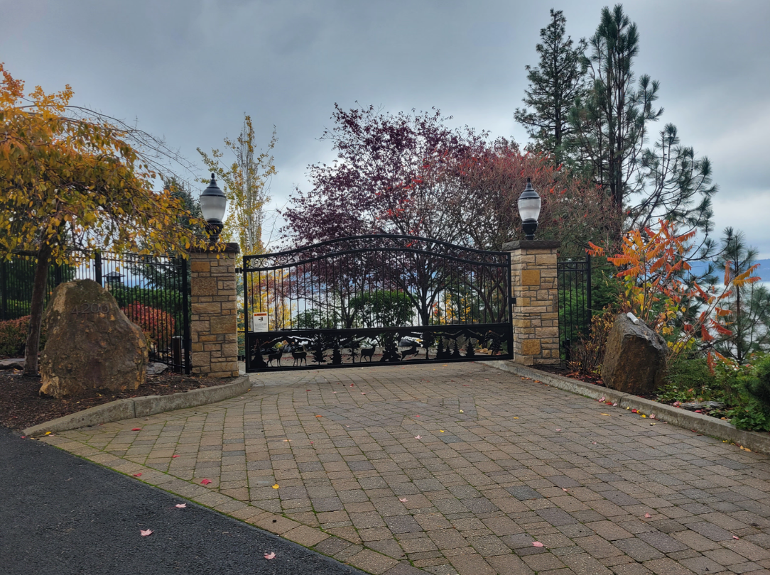 Enhance Access and Security with an Automatic Gate Ornate black gate with stone pillars and brick driveway, trees with autumn colors in background.