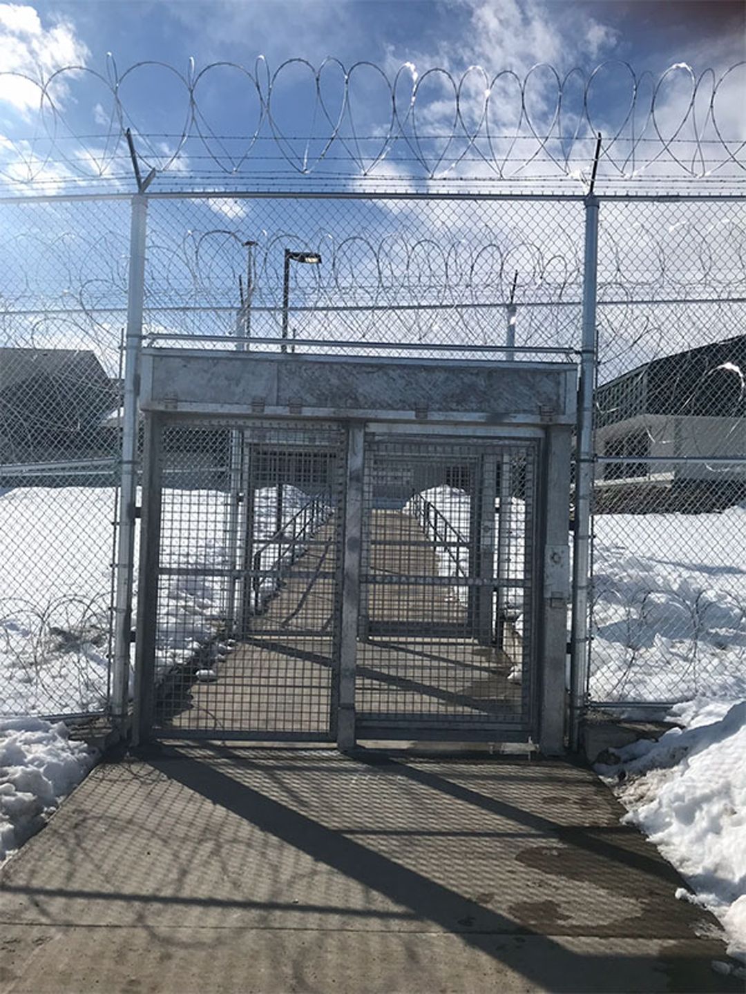 A barbed wire fence surrounds a walkway leading to a prison.