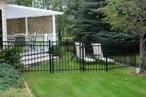 A black metal fence surrounds a lush green yard in front of a house.