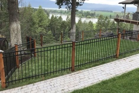 A metal fence with wooden posts is surrounding a lush green field.