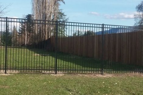 A metal fence is surrounding a wooden fence in a yard.