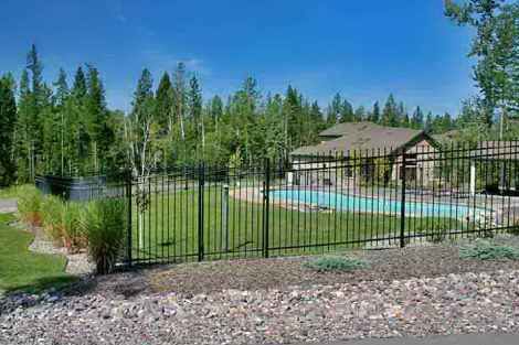 A fence surrounds a swimming pool with a house in the background.