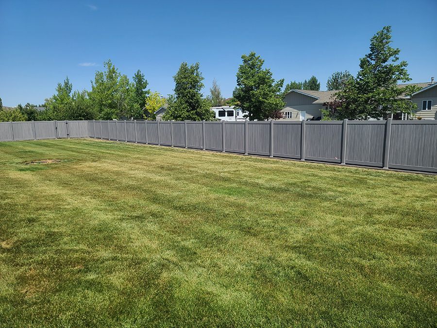 A fence surrounds a lush green field with a house in the background.