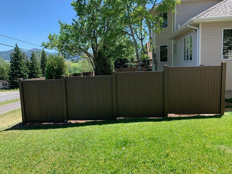 A brown fence is sitting in the grass in front of a house.