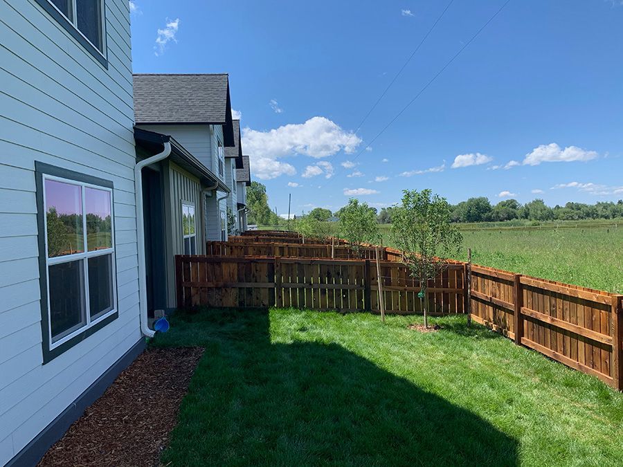 A backyard with a wooden fence and a house in the background.