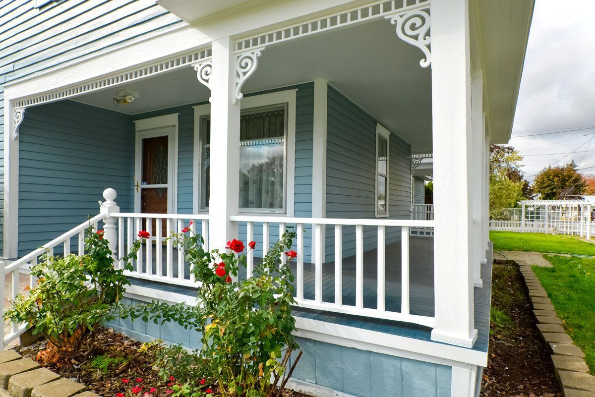 A blue house with a white porch and flowers in front of it.
