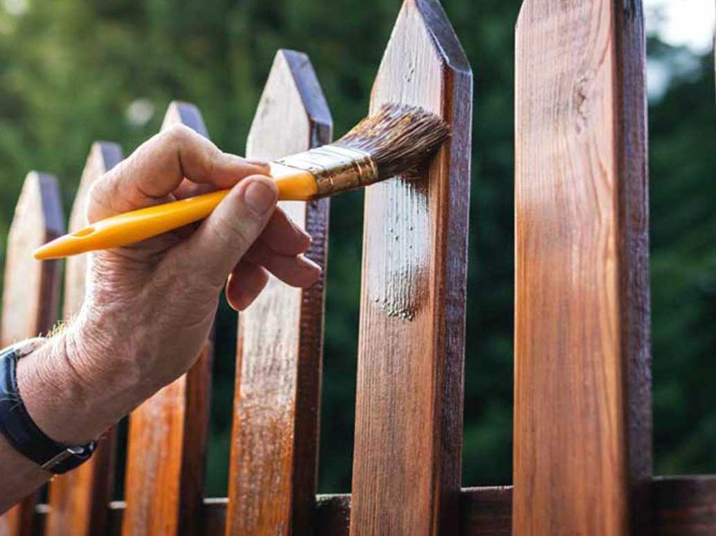 A person is painting a wooden fence with a brush.