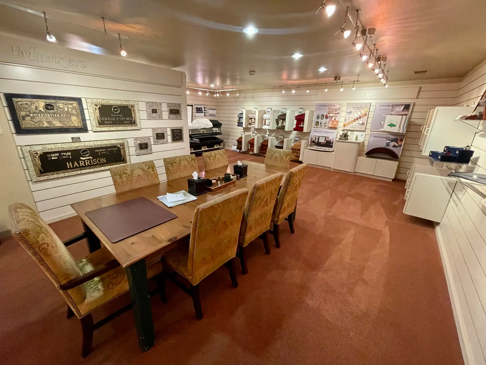A conference room with a wooden table, chairs, and display cases, lit by overhead track lighting.