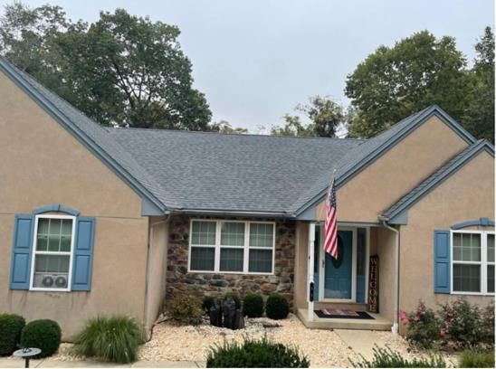 Beige house with blue trim, gray roof, American flag, and stone facade around the front door.
