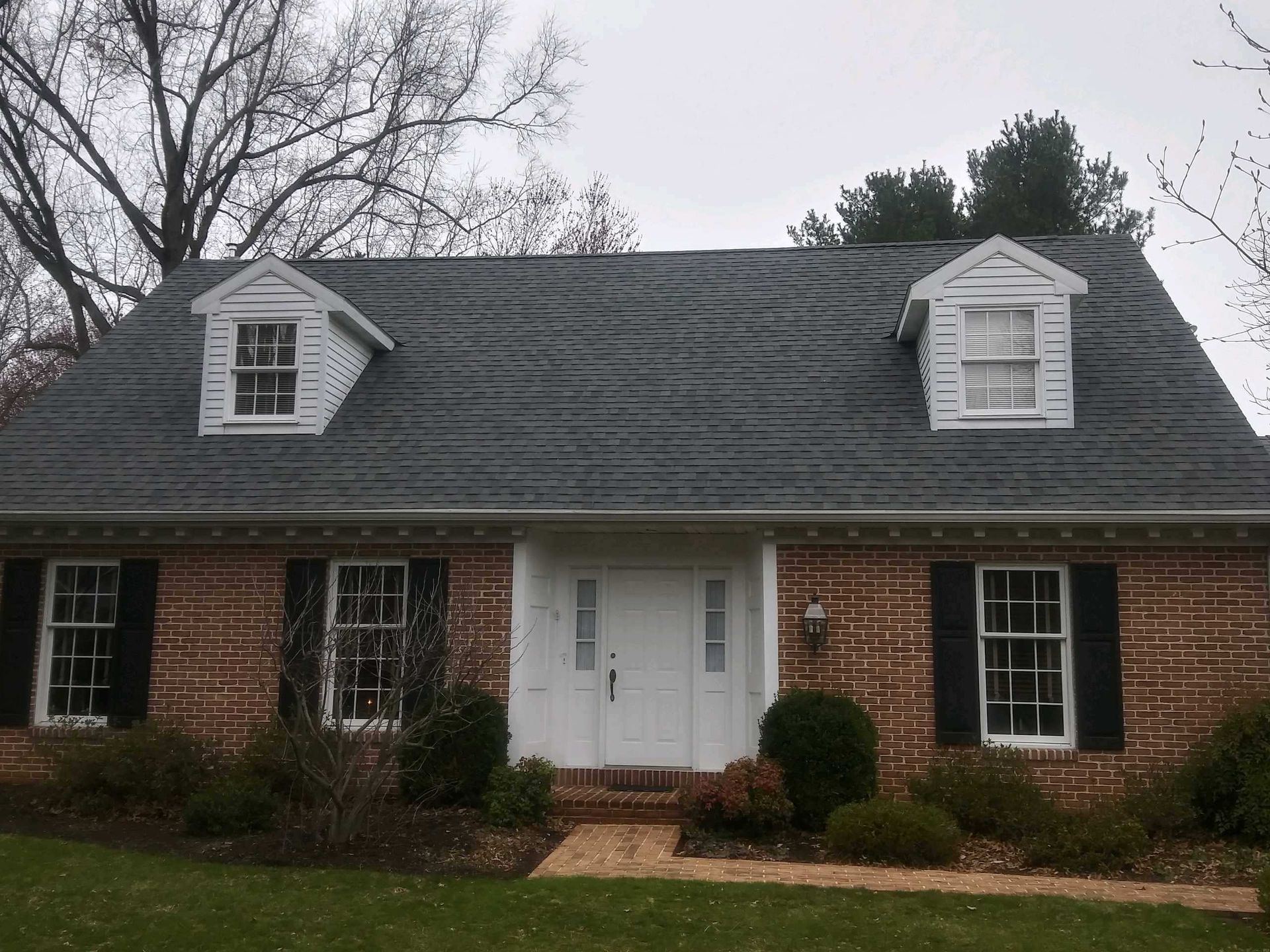 Brick house with a dark roof and two white dormers on a cloudy day.