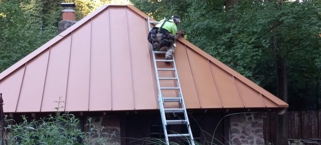 A person climbs a ladder to a copper-colored roof of a small building.